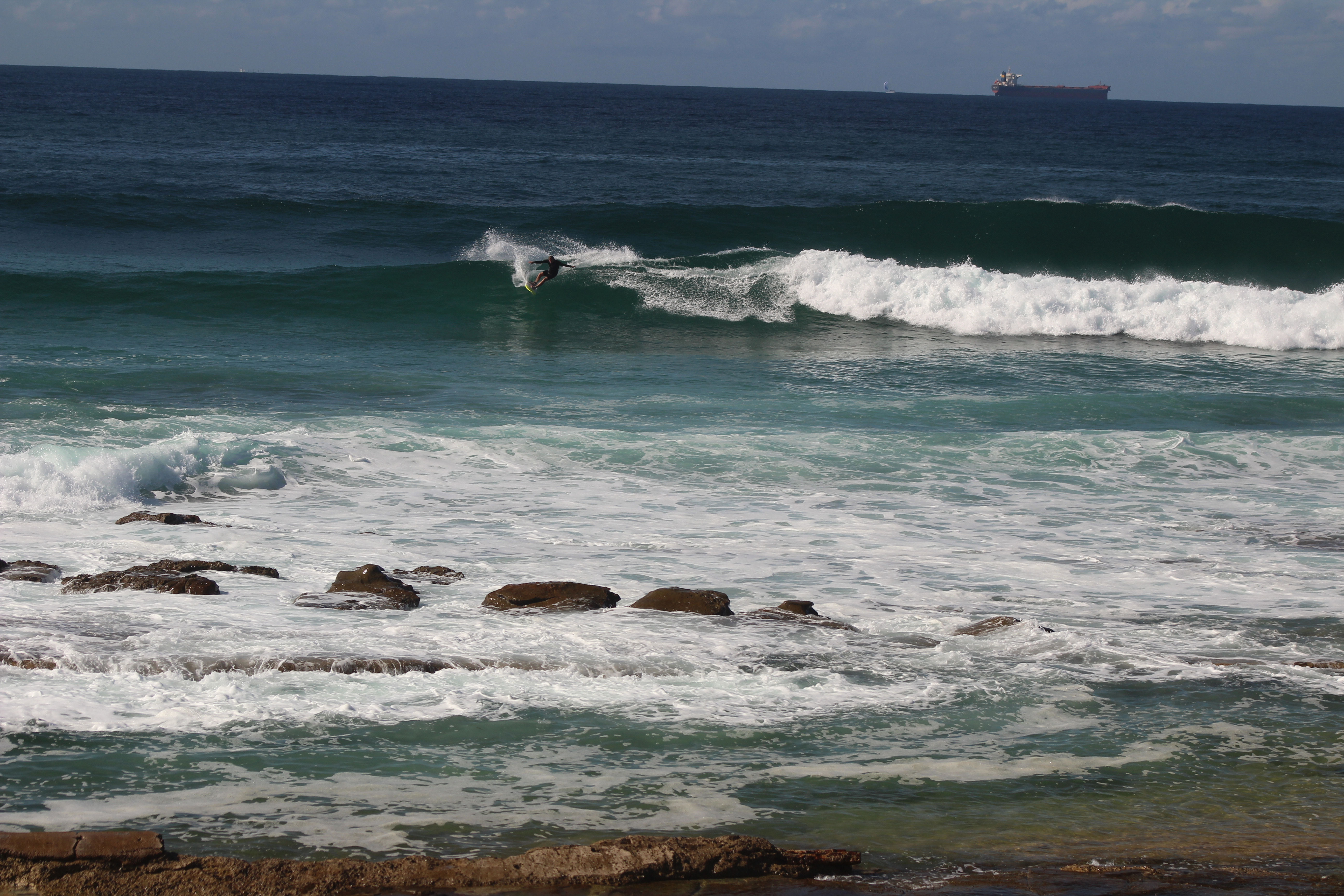 surfer surfing at Dixon Park Beach with breaking waves and rocks near the beach