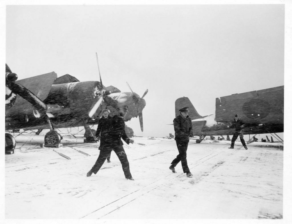 Snowball fight on the deck of HMS Emperor in front of Hellcat fighters