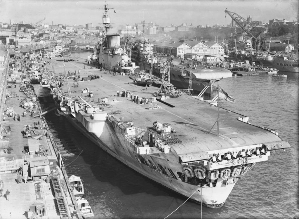 HMS Indefatigable at wharf Number 1 Woolloomooloo. At Wharf Numbers 6-9 are two other Royal Navy large fleet aircraft carriers Dated c.1946