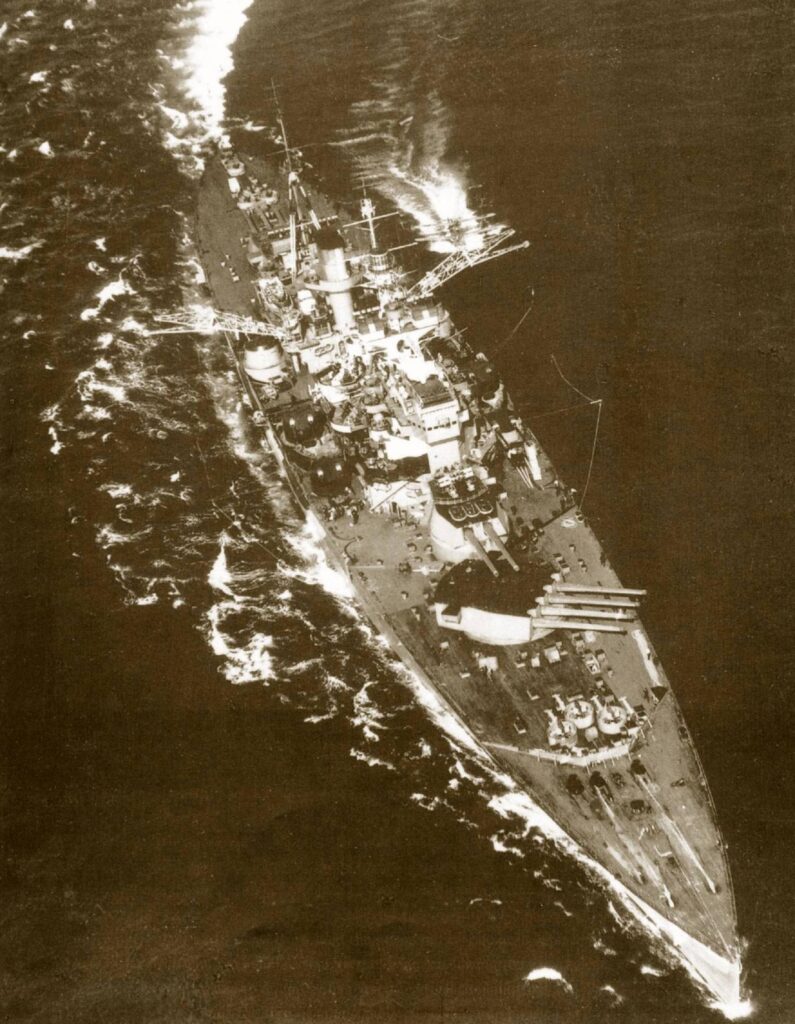 HMS Anson in a turn to port as she recovers one of her Supermarine Walrus