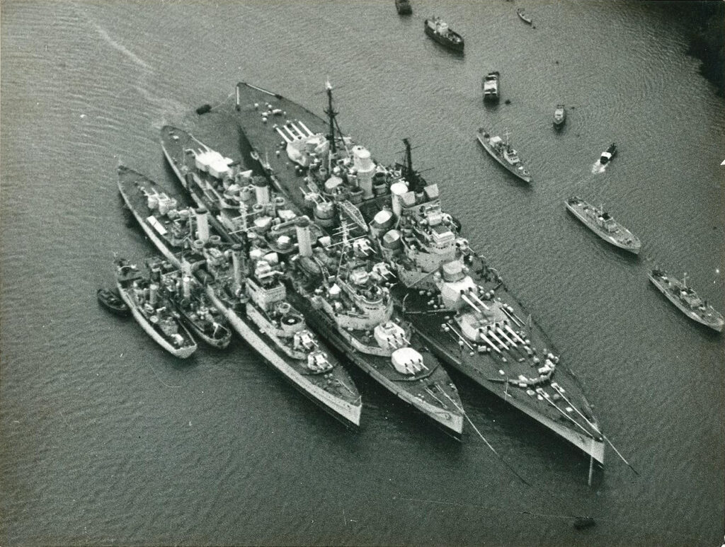 HMS Howe, cruiser HMS Belfast and a Dido class cruiser, which is possibly HMS Euryalus, in reserve at Devonport c. 1954-55